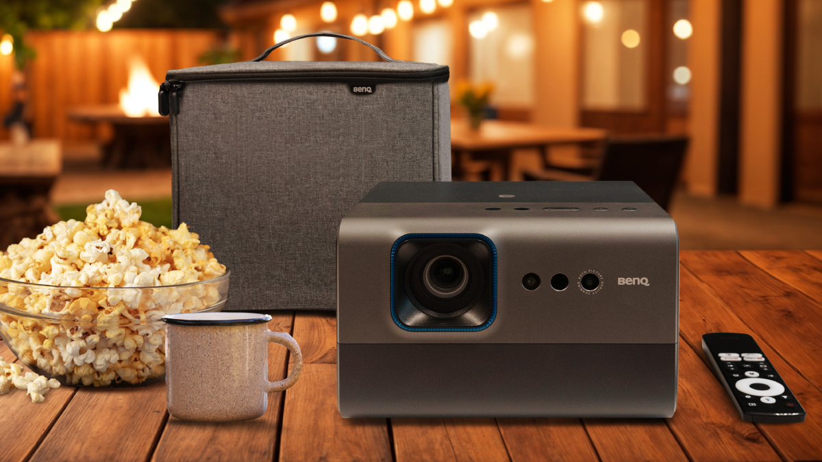 Vidéoprojecteur BenQ GP520 et étui de transport sur une table en bois dans un jardin, entourés de pop-corn et d'une tasse, démontrant portabilité et divertissement