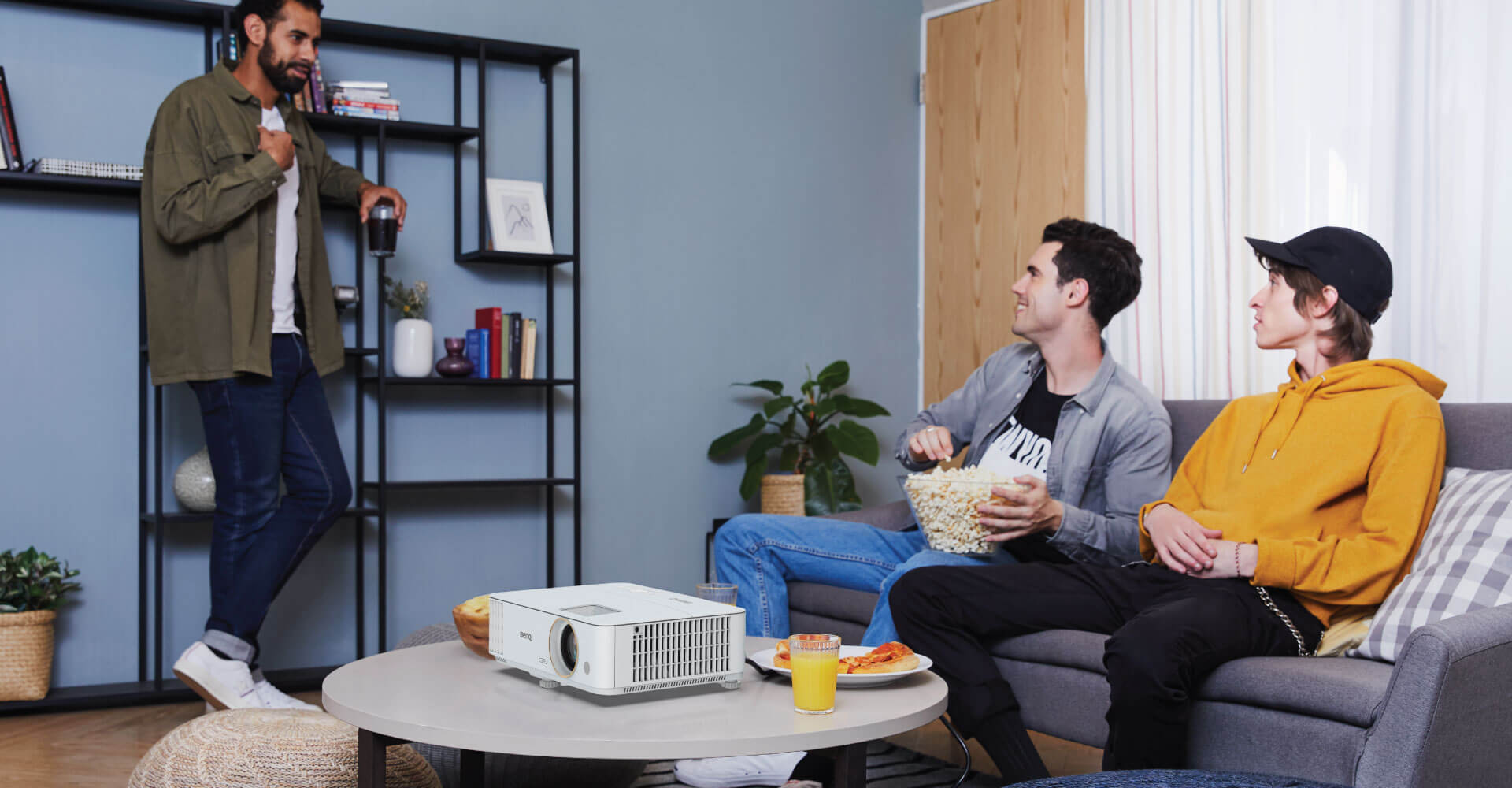 Tres hombres teniendo una pequeña charla en la sala de estar con palomitas de maíz, con el proyector sobre la mesa